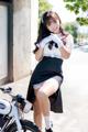 A woman in a maid outfit posing next to a motorcycle.