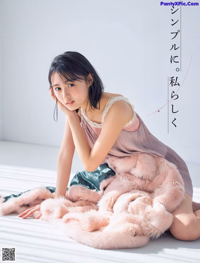 A woman sitting on a bed covered in a pink fur blanket.