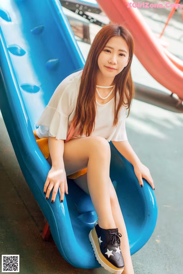 A young woman sitting on a blue slide.
