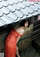 A woman in a red dress leaning against a wall.