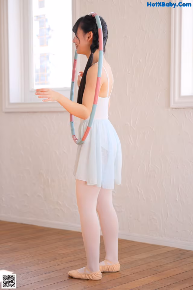 A young girl in a white dress holding a hula hoop.