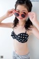 A young girl wearing a black and white polka dot bikini and heart shaped sunglasses.