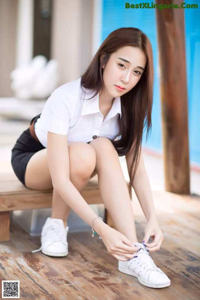 A woman sitting on a wooden bench tying up her shoes.