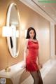 A woman in a red dress standing in front of a mirror.