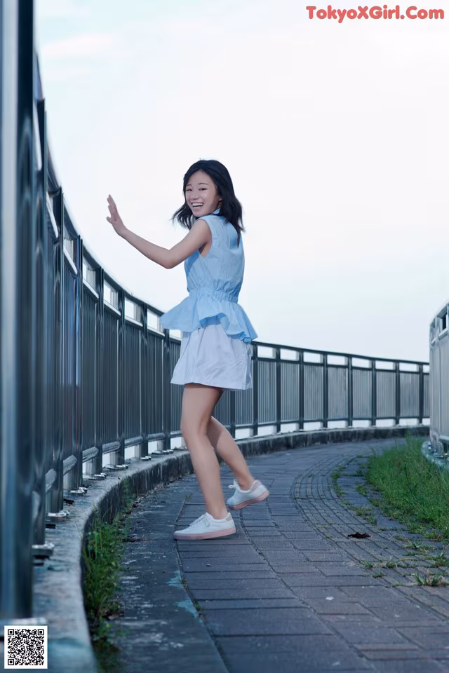 A woman in a blue dress is standing on a bridge.
