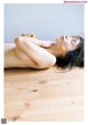 A naked woman laying on a wooden floor with her eyes closed.