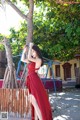 A woman in a red dress leaning against a tree.