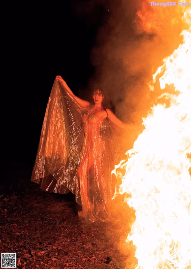 A woman standing in front of a fire in the dark.