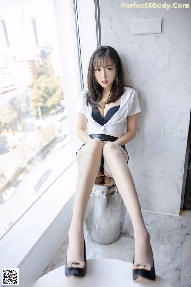 A woman sitting on top of a stool next to a window.
