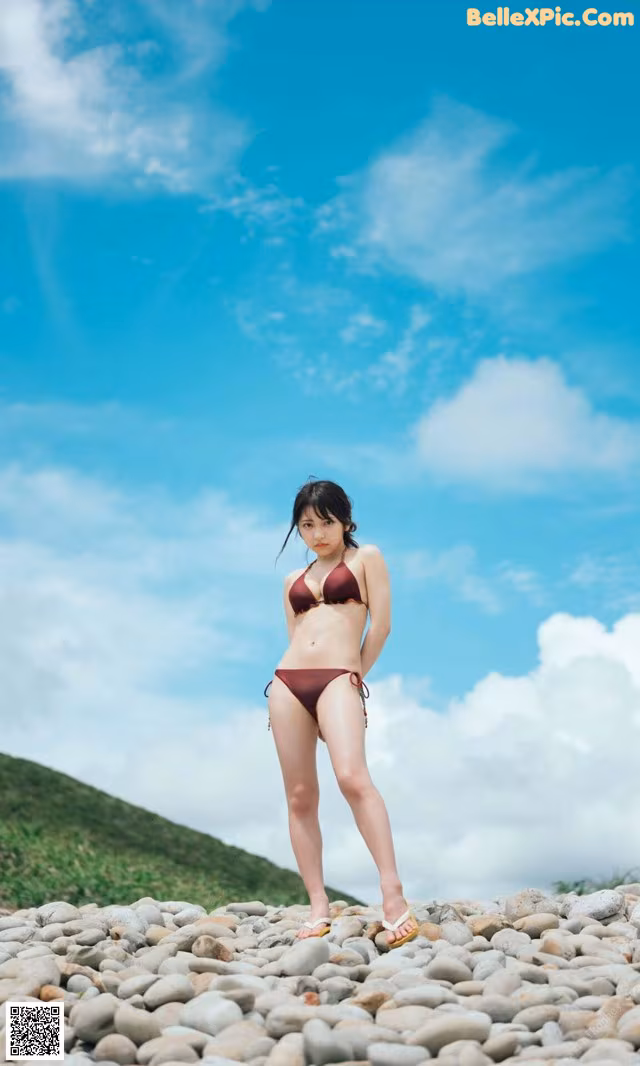 A woman in a bikini standing on a rocky beach.