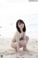 A woman in a bikini sitting on the beach.