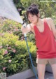 A woman in a red tank top is holding a hose.