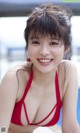 A woman in a red bikini posing by a pool.